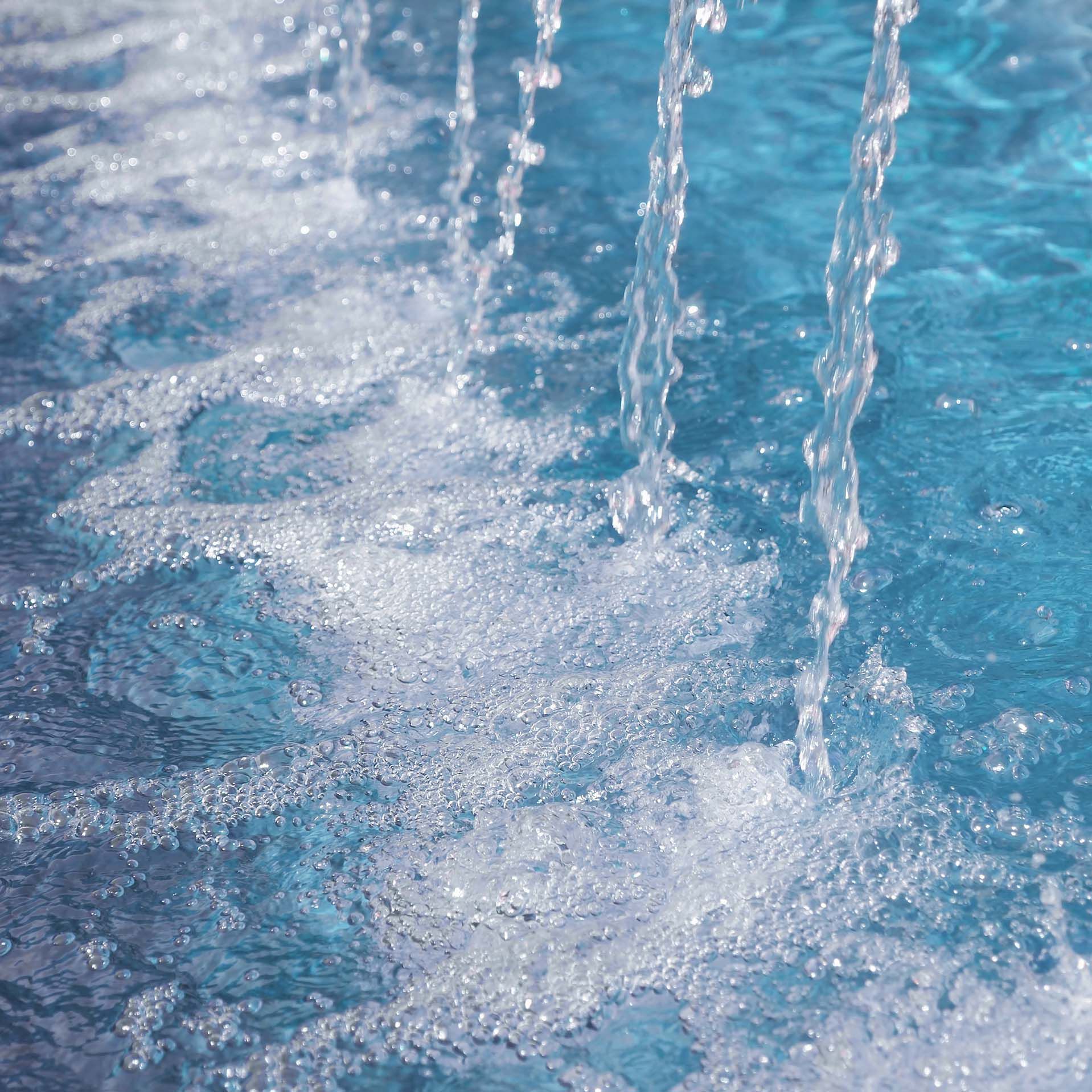 Stream of water pouring into pool of blue water with bubbles